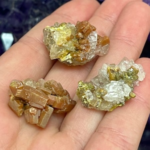 May include: Three small clusters of brown, green, and clear crystals. The crystals are arranged in a cluster and have a rough, natural texture.