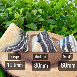 May include: Three stone pyramids in varying sizes, each with a unique pattern of cream, black, and grey veining. The largest is 100mm, the medium is 80mm, and the smallest is 60mm. The pyramids are displayed on a wooden surface.