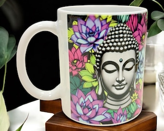 May include: White ceramic mug featuring a serene Buddha image surrounded by colorful lotus flowers in pink, purple, and green. The mug has a curved handle and sits on a small, square wooden coaster.