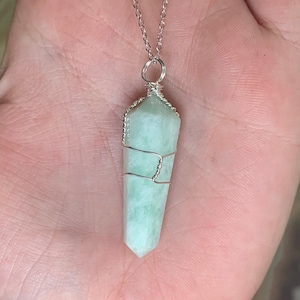 May include: A silver chain necklace with a light green crystal pendant wrapped in silver wire.