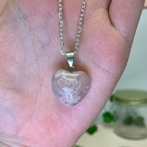 Puede incluir: Un collar de cadena de plata con un colgante en forma de coraz&oacute;n hecho de &aacute;gata rosa y blanca.