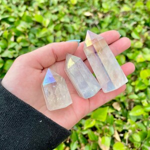 K&ouml;nnte beinhalten: Drei regenbogenfarbene, klare Quarzkristallspitzen mit einem regenbogenfarbenen Schimmer. Die Spitzen haben unterschiedliche Gr&ouml;&szlig;en und werden in einer Hand gehalten.