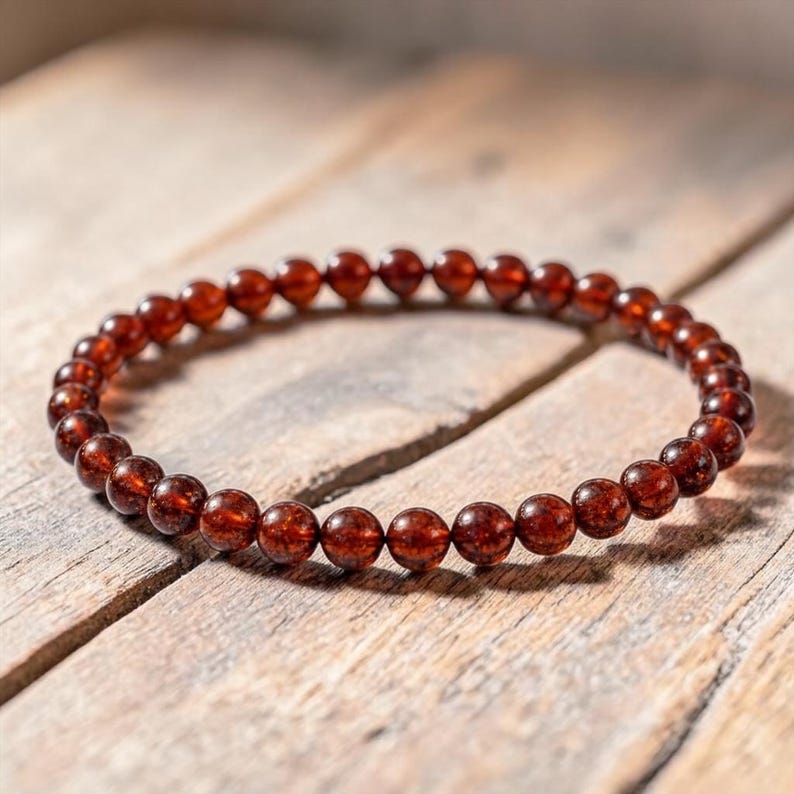 May include: A beaded bracelet featuring small, round, dark red beads. The bracelet is resting on a weathered wooden surface, with the beads reflecting light. The bracelet is a jewelry item.
