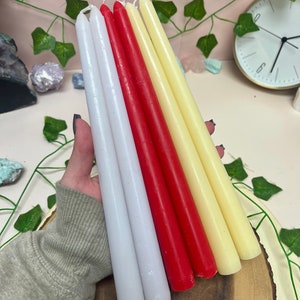 May include: A set of six taper candles in white, cream, and red. The candles are arranged in a fan shape and are sitting on a wooden surface.