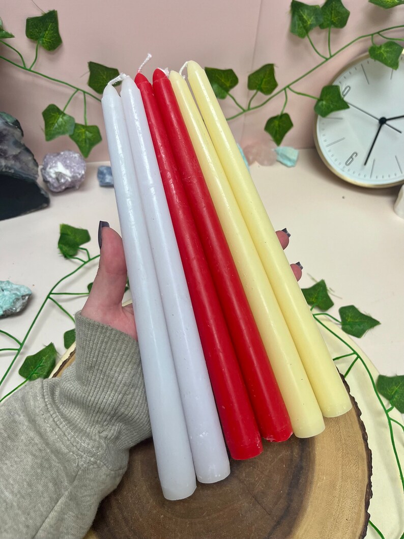 May include: A set of six taper candles in white, cream, and red. The candles are arranged in a fan shape and are sitting on a wooden surface.