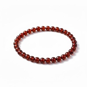 May include: A bracelet made of small, round, reddish-brown beads. The beads are strung together to form a circular shape. The bracelet is set against a plain white background.