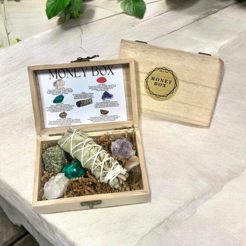 Peut inclure: Une bo&icirc;te en bois avec l'inscription "Money Box" sur le couvercle. La bo&icirc;te contient une vari&eacute;t&eacute; de cristaux, dont du quartz clair, de l'am&eacute;thyste, de la cornaline, de la pyrite et de l'aventurine verte. Il y a aussi un b&acirc;tonnet de sauge blanche.