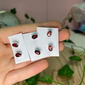 May include: Three pairs of silver stud earrings with red oval-shaped gemstones. The earrings are displayed on white cards.
