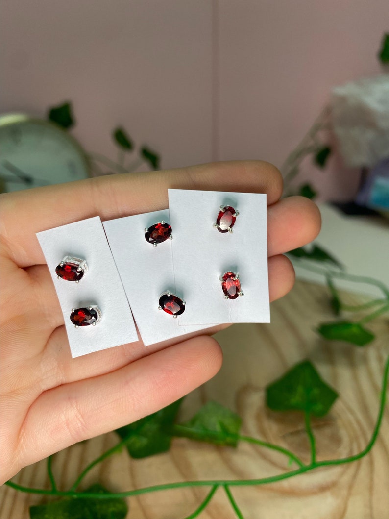 May include: Three pairs of silver stud earrings with red oval-shaped gemstones. The earrings are displayed on white cards.