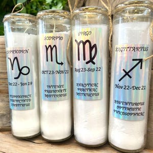 Puede incluir: Cuatro tarros de velas de vidrio con velas blancas y signos del zod&iacute;aco y fechas impresos en el frente. Los signos son Capricornio, Escorpio, Virgo y Sagitario.