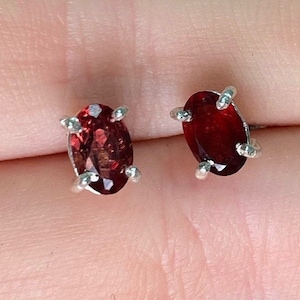 May include: A pair of silver stud earrings with oval-shaped red gemstones.