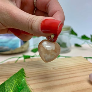 Puede incluir: Un colgante de coraz&oacute;n de &aacute;gata con un patr&oacute;n blanco y marr&oacute;n. El colgante est&aacute; colgado de una cadena de plata.