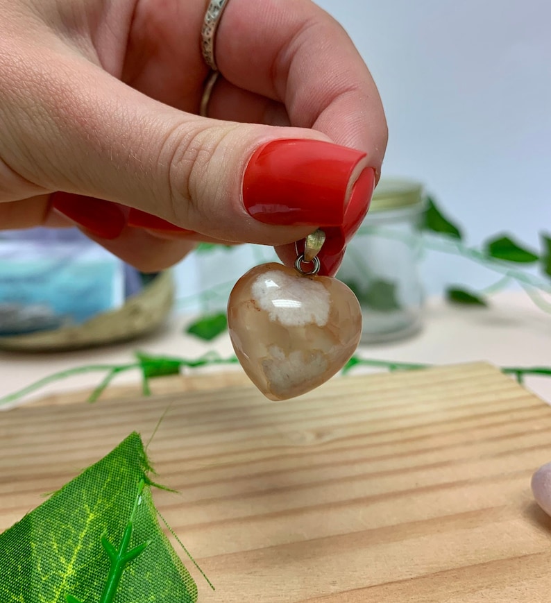Puede incluir: Un colgante de coraz&oacute;n de &aacute;gata con un patr&oacute;n blanco y marr&oacute;n. El colgante est&aacute; colgado de una cadena de plata.