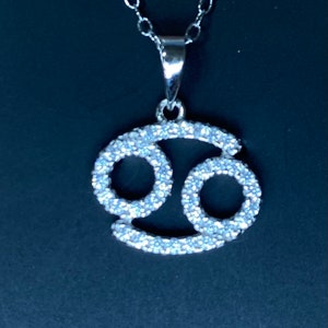 May include: Silver pendant necklace featuring a Cancer zodiac sign with a sparkling crystal design.