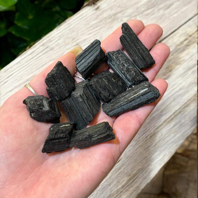 May include: A collection of black tourmaline crystals, also known as schorl, in various sizes and shapes. The crystals have a dark, opaque appearance and a striated texture.
