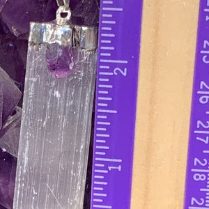 May include: A silver chain necklace with a white selenite crystal pendant and a small amethyst crystal. The pendant is approximately 1.5 inches long. The necklace is displayed on a bed of amethyst crystals.
