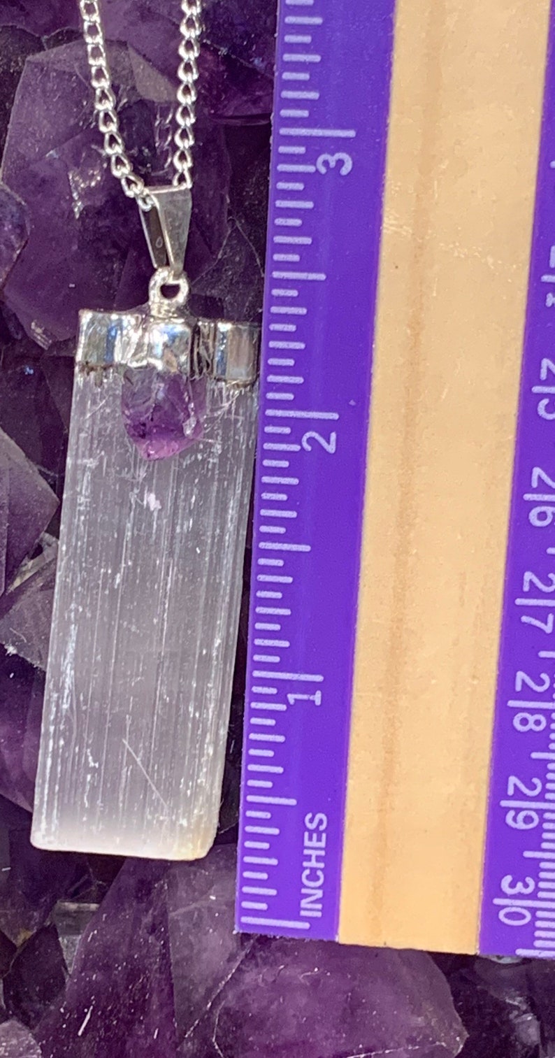 May include: A silver chain necklace with a white selenite crystal pendant and a small amethyst crystal. The pendant is approximately 1.5 inches long. The necklace is displayed on a bed of amethyst crystals.