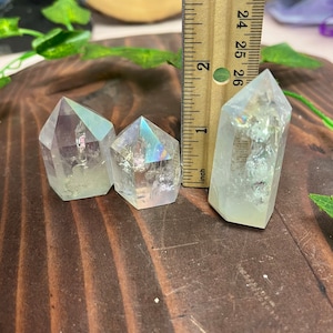 K&ouml;nnte beinhalten: Drei regenbogenfarbene, klare Quarzkristallspitzen in verschiedenen Gr&ouml;&szlig;en auf einer Holzoberfl&auml;che. Die Kristalle sind etwa 2,5 cm, 3,8 cm und 5 cm hoch.