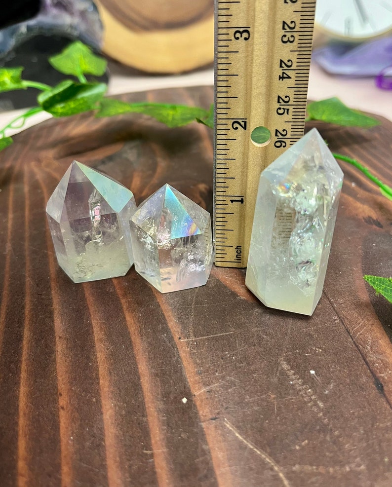K&ouml;nnte beinhalten: Drei regenbogenfarbene, klare Quarzkristallspitzen in verschiedenen Gr&ouml;&szlig;en auf einer Holzoberfl&auml;che. Die Kristalle sind etwa 2,5 cm, 3,8 cm und 5 cm hoch.