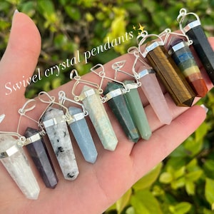 May include: A collection of 10 crystal pendants with silver swivel clasps. The crystals are in various colors and shapes, including clear, white, grey, green, blue, pink, brown, red, and black.