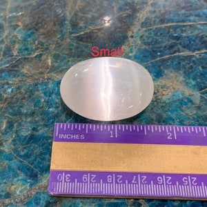 K&ouml;nnte beinhalten: Ein kleiner, wei&szlig;er, ovaler Selenitkristall mit schimmerndem, irisierendem Glanz. Der Kristall ist etwa 2,5 cm lang und liegt auf einem Lineal zur Gr&ouml;&szlig;enreferenz.