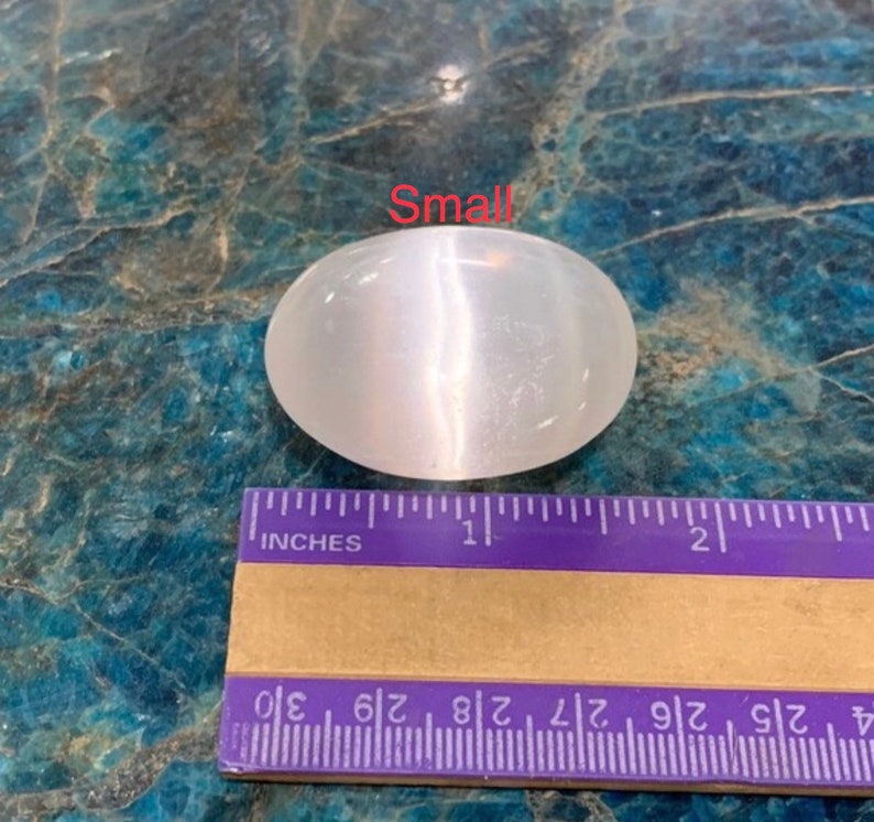 K&ouml;nnte beinhalten: Ein kleiner, wei&szlig;er, ovaler Selenitkristall mit schimmerndem, irisierendem Glanz. Der Kristall ist etwa 2,5 cm lang und liegt auf einem Lineal zur Gr&ouml;&szlig;enreferenz.
