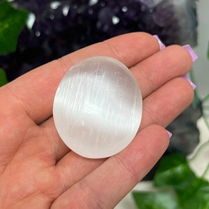 K&ouml;nnte beinhalten: Ein wei&szlig;er Selenit-Handstein mit einer glatten, gestreiften Oberfl&auml;che. Der Stein wird in einer Hand gehalten.