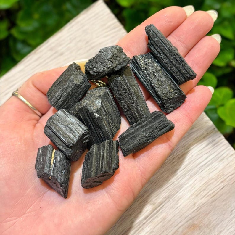 May include: A collection of black tourmaline crystals, also known as schorl, in various sizes and shapes. The crystals have a dark, opaque appearance and a striated texture.