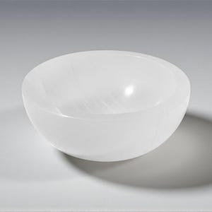 May include: A white, oval bowl with a smooth, polished surface. The bowl is made of a translucent material, and it casts a shadow on the surface below. The bowl is likely used for decorative purposes.
