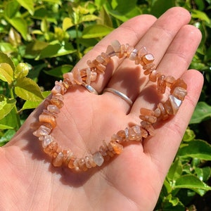 May include: A sunstone chip bracelet with a mix of orange, brown, and white chips. The bracelet is made of natural stones and is strung on elastic.
