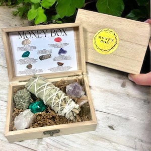 Peut inclure: Une bo&icirc;te en bois avec un couvercle qui s'ouvre pour r&eacute;v&eacute;ler une vari&eacute;t&eacute; de cristaux et un paquet de sauge. La bo&icirc;te est &eacute;tiquet&eacute;e "Money Box" et comprend une liste des cristaux et de leurs propri&eacute;t&eacute;s. Les cristaux comprennent le quartz clair, l'aventurine verte, l'am&eacute;thyste, la pyrite, l'&oelig;il de tigre et la cornaline.