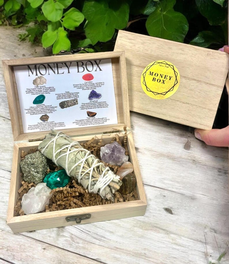 Peut inclure: Une bo&icirc;te en bois avec un couvercle qui s'ouvre pour r&eacute;v&eacute;ler une vari&eacute;t&eacute; de cristaux et un paquet de sauge. La bo&icirc;te est &eacute;tiquet&eacute;e "Money Box" et comprend une liste des cristaux et de leurs propri&eacute;t&eacute;s. Les cristaux comprennent le quartz clair, l'aventurine verte, l'am&eacute;thyste, la pyrite, l'&oelig;il de tigre et la cornaline.