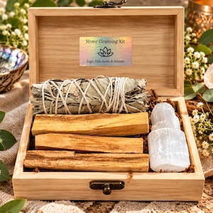 Könnte beinhalten: Eine helle Holzschachtel mit einem Reinigungsset. Darin befinden sich ein mit weißer Schnur gebundenes Salbei-Bündel, drei rechteckige Palo-Santo-Holzstäbchen und ein weißer Selenit-Kristall. Ein Etikett trägt die Aufschrift Home Cleansing Kit Sage, Palo Santo & Selenite.