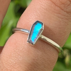 May include: A silver ring with a blue iridescent coffin-shaped gemstone.