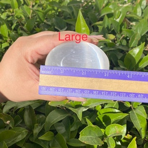 K&ouml;nnte beinhalten: Eine gro&szlig;e, wei&szlig;e Selenitkugel mit einem Durchmesser von etwa 5 cm. Die Kugel ist glatt und poliert und hat einen leichten Glanz. Das Wort "Large" ist in roter Schrift &uuml;ber der Kugel geschrieben.