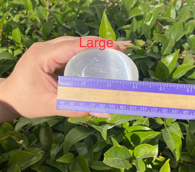 K&ouml;nnte beinhalten: Eine gro&szlig;e, wei&szlig;e Selenitkugel mit einem Durchmesser von etwa 5 cm. Die Kugel ist glatt und poliert und hat einen leichten Glanz. Das Wort "Large" ist in roter Schrift &uuml;ber der Kugel geschrieben.