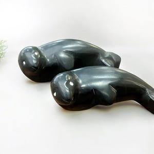May include: Two black carved sculptures of seals, each with white eyes, lying on a white surface.