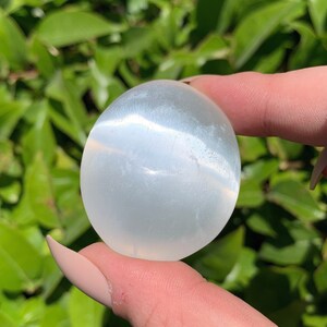 K&ouml;nnte beinhalten: Ein glattes, wei&szlig;es Selenit-Ei mit einem subtilen Schimmer. Das Ei ist etwa so gro&szlig; wie ein Golfball und wird in einer Hand gehalten.