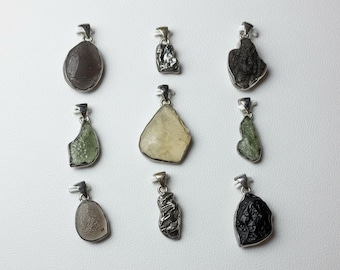 May include: Nine gemstone pendants with silver-colored metal findings. The pendants feature various shapes and colors, including brown, green, and black. The gemstones are set in a silver-colored metal. The pendants are displayed on a white surface.