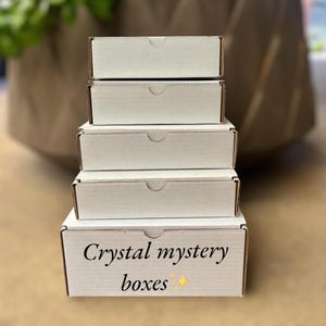 May include: A stack of five white boxes with the words "Crystal mystery boxes" printed on the bottom box.