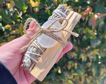 May include: A bundle of white sage and palo santo sticks tied together with twine and a clear quartz crystal.