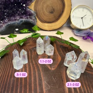 K&ouml;nnte beinhalten: Sechs regenbogenfarbene, klare Quarzkristallspitzen in verschiedenen Gr&ouml;&szlig;en auf einer Holzoberfl&auml;che. Die Kristalle sind in drei Gruppen angeordnet, mit dem Text .5-1 oz, 1.1-2 oz und 2.1-3 oz unter jeder Gruppe.