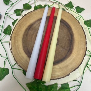 May include: Three taper candles on a wooden slice. The candles are white, red, and cream.