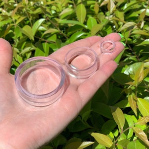 May include: Three clear plastic rings of different sizes, held in a hand. The rings are smooth and translucent.