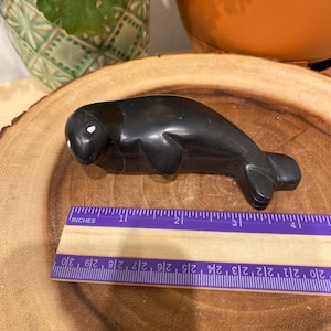 May include: A black carved walrus figurine with white eyes. The figurine is approximately 3 inches long and is sitting on a wooden surface.
