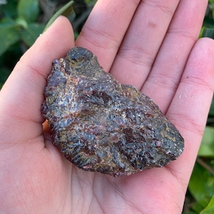May include: A dark red and black rough, natural, raw, unpolished, gemstone. The stone has a rough, irregular shape and is a dark red color with black flecks throughout.