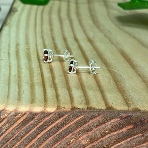 May include: A pair of silver stud earrings with small, oval-shaped red gemstones set in a cage-like design.