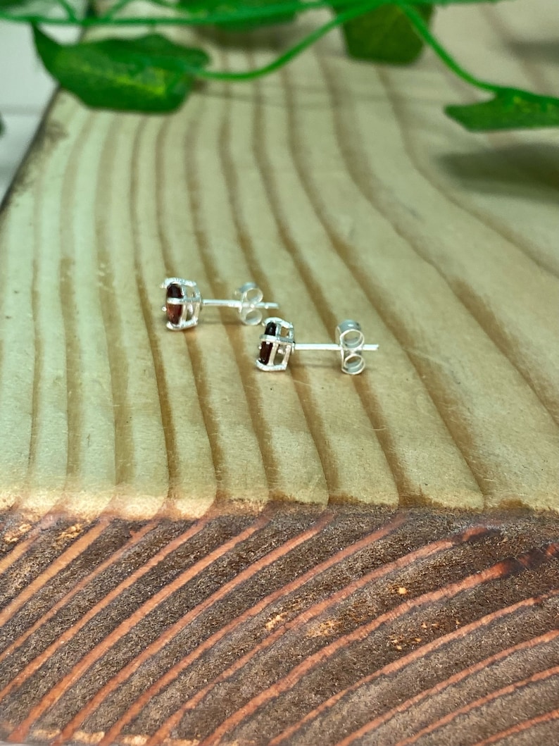 May include: A pair of silver stud earrings with small, oval-shaped red gemstones set in a cage-like design.