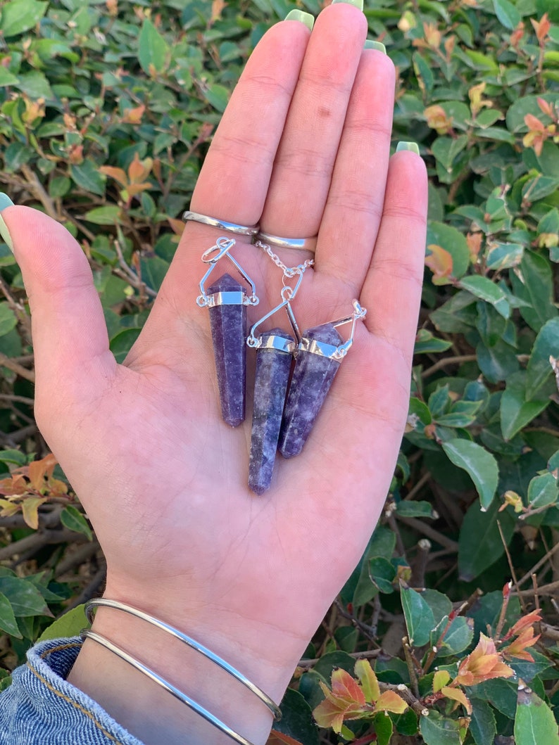 May include: Three purple amethyst crystal point pendants with silver chain and bail. The pendants are held in a hand.