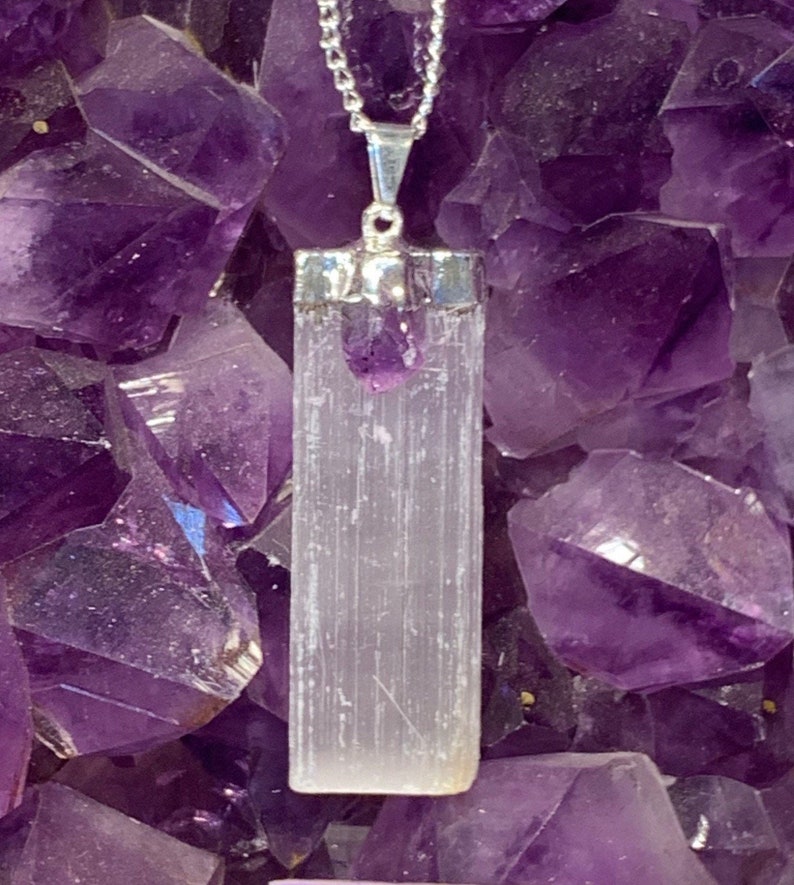 May include: A silver chain necklace with a white selenite crystal pendant and a small amethyst crystal at the top. The pendant is set in a silver bezel and hangs from a silver chain.